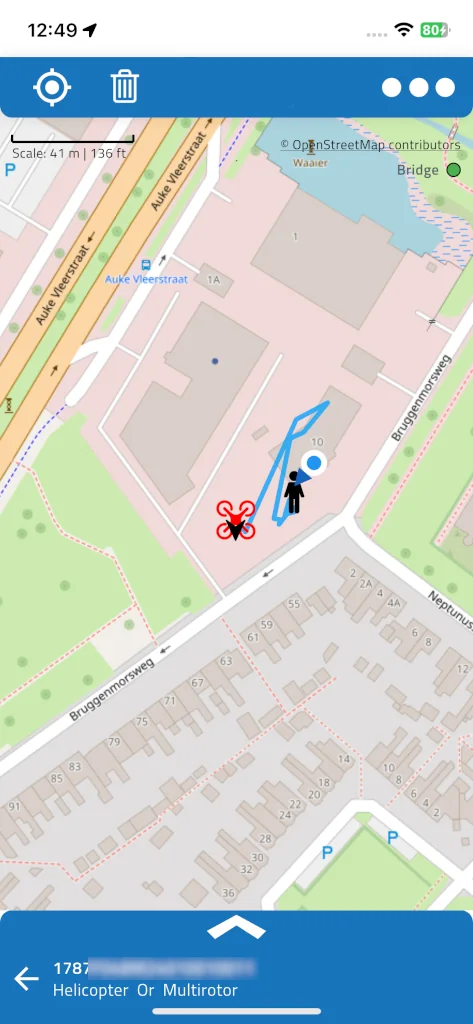 A selected drone shown as a red icon, with its light-blue track, the black pilot icon next to it and the blue dot of the phone's own position